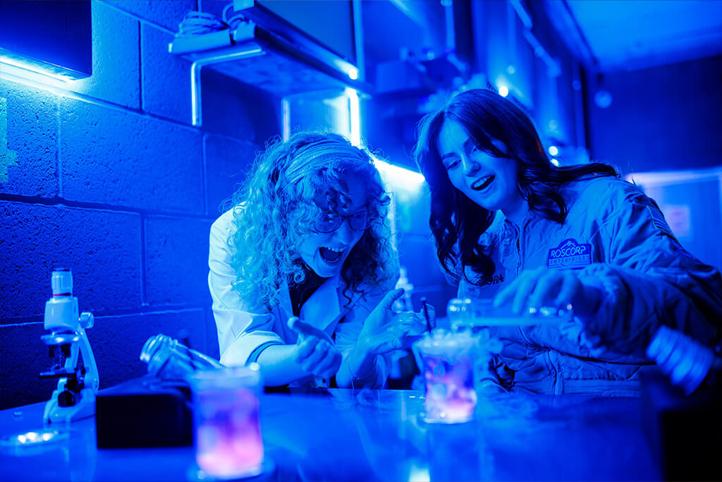 Guests enjoying cocktails inside Avora's immersive laboratory set with futuristic design and lighting.